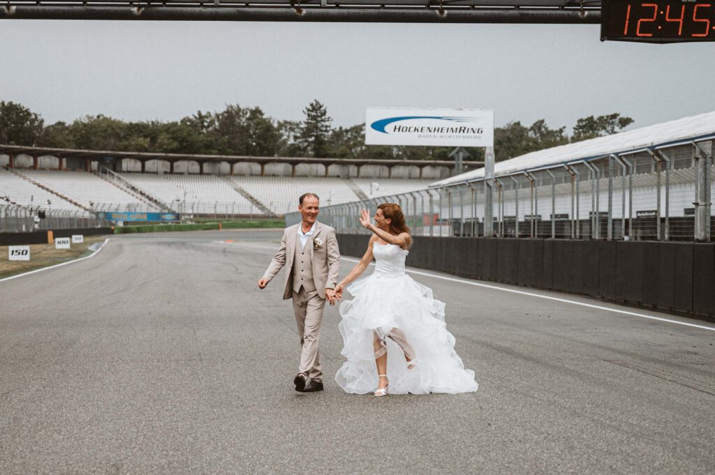 Hochzeit Hockenheimring - BrautpaarShooting Brautpaar laeuft und winkt auf Rennstrecke