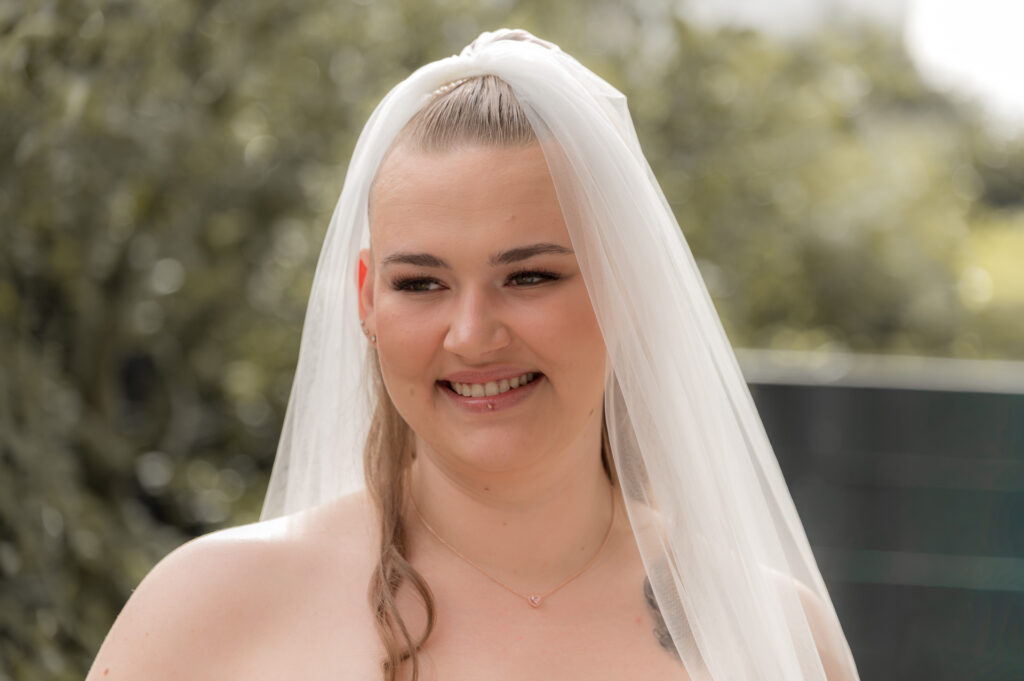 Braut steht mit Schleier im freien und strahlt